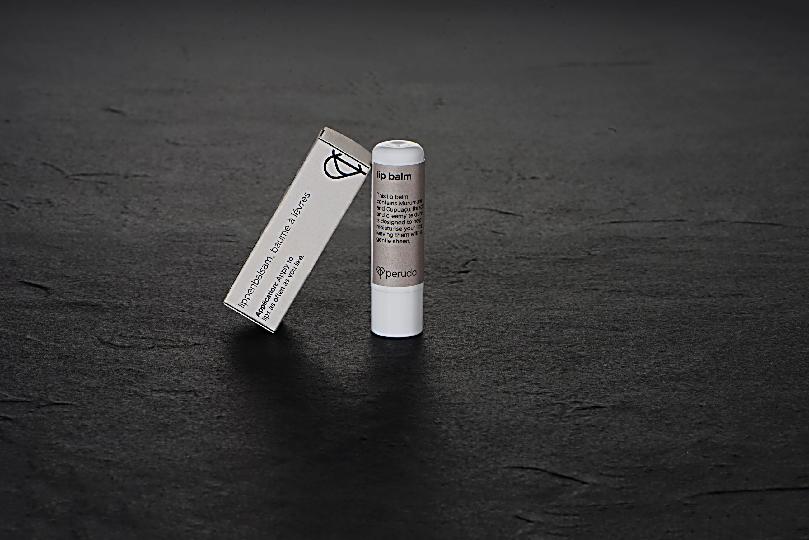 Peruda lip balm in a white tube next to a beige box.