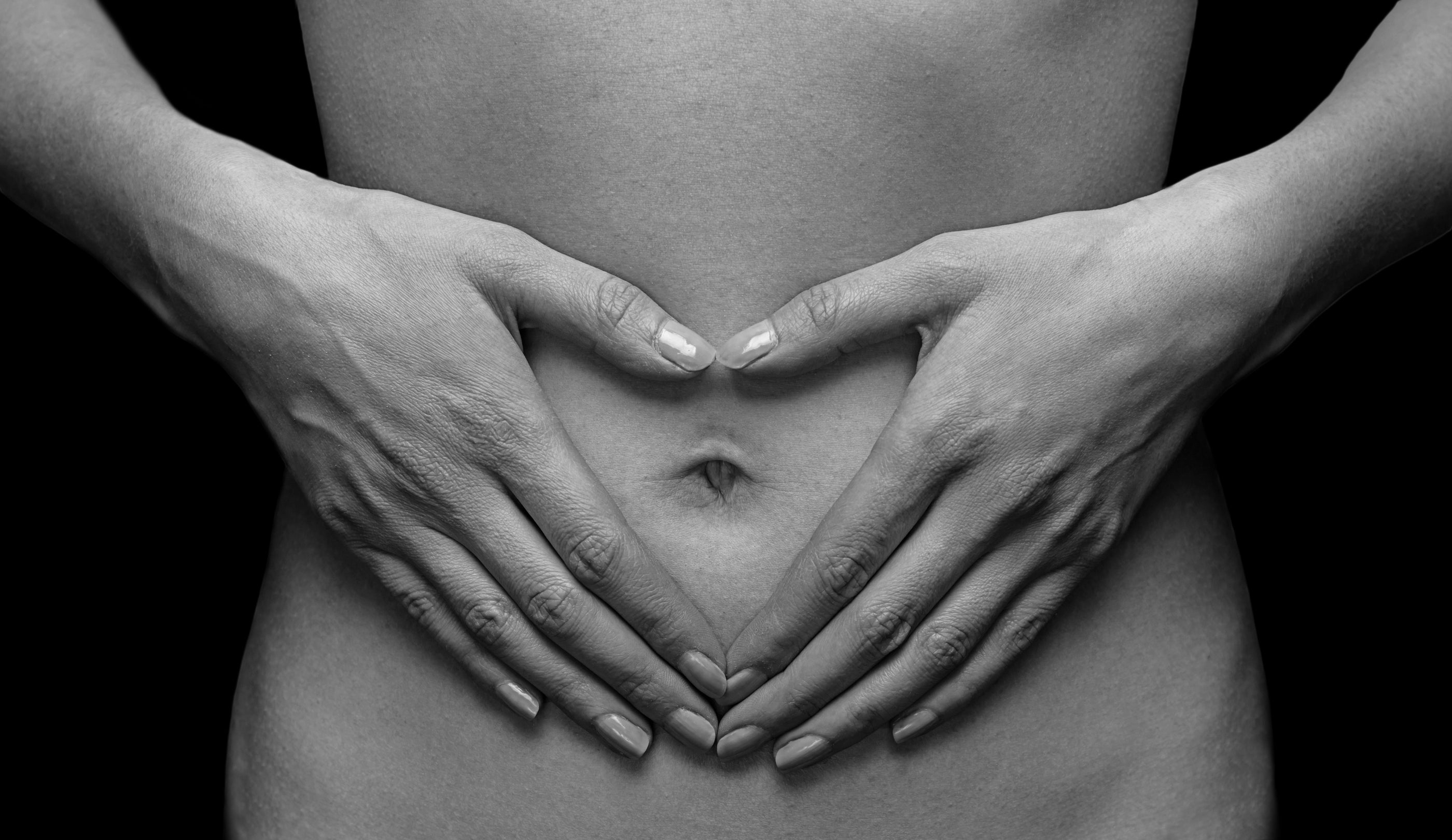 Black and white image of hands forming a heart shape over a pregnant belly.