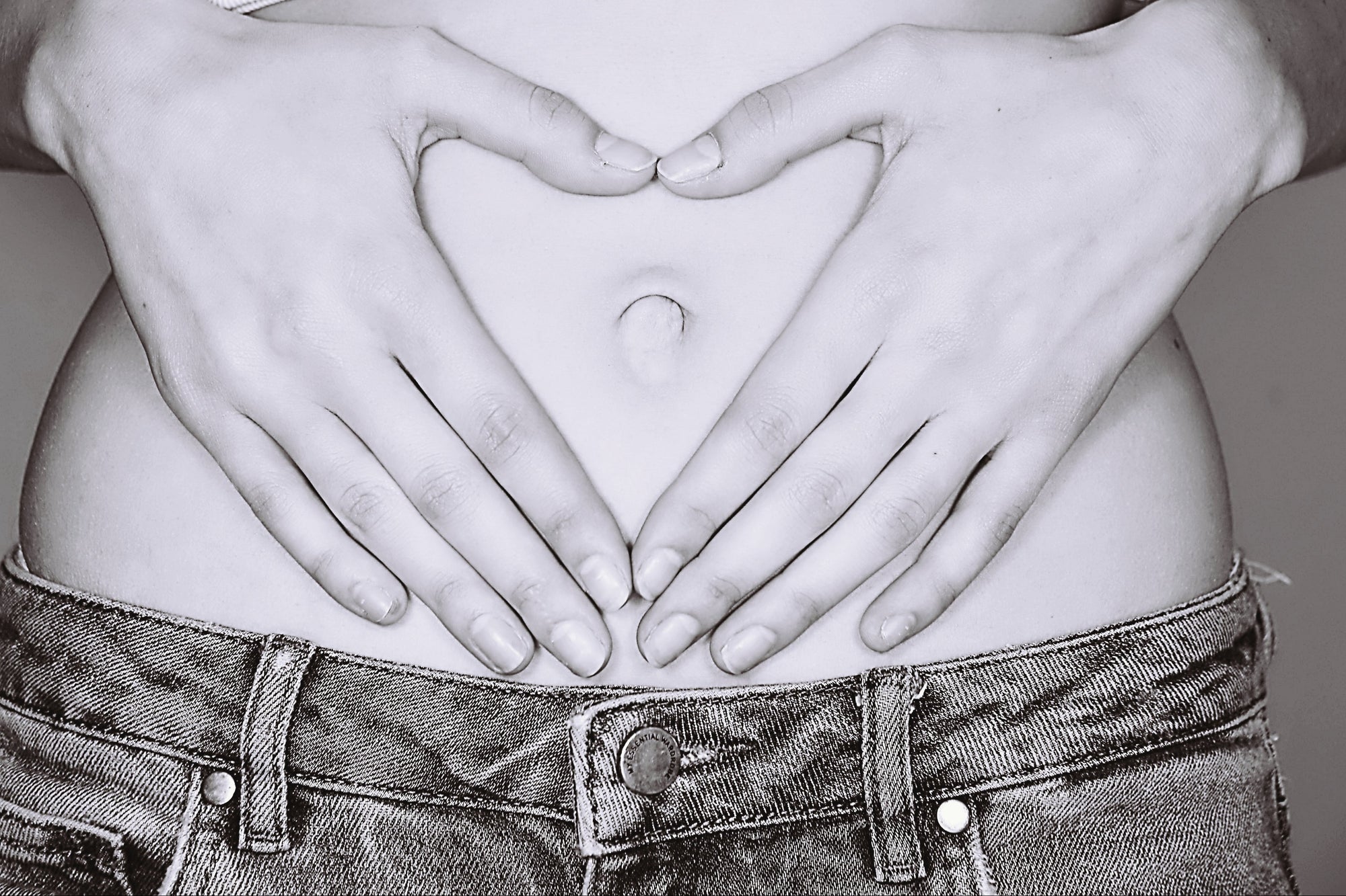 Person with hands forming a heart shape over a bare stomach, likely indicating pregnancy.