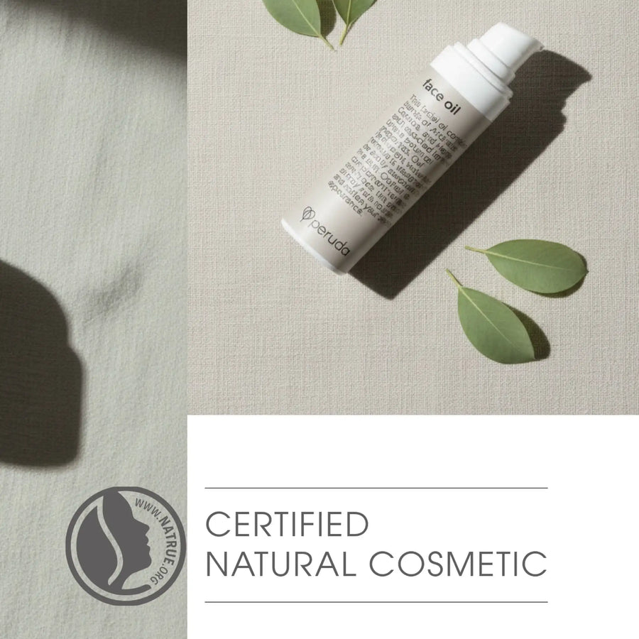 A white tube of face oil lies diagonally on a light beige textured fabric surface with a few green leaves around it. The lower portion of the image has a white panel with the text 'CERTIFIED NATURAL COSMETIC' and a circular logo reading 'www.