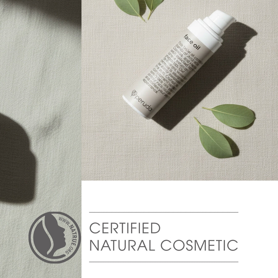 Peruda face oil flatlay on a linen cloth with leaves and NATRUE-certification logo