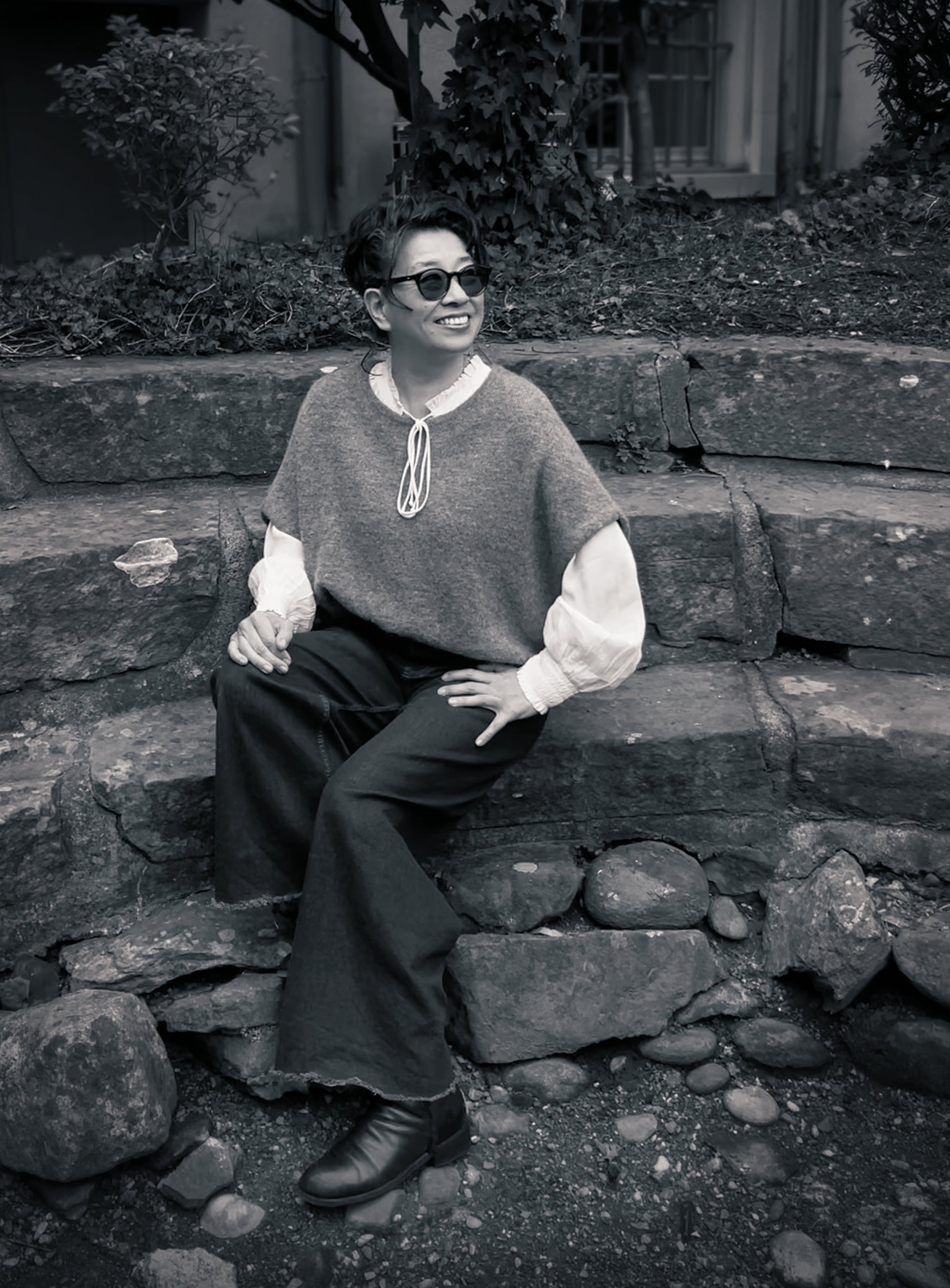 Monica Otten smiling, sitting on a stone garden wall.