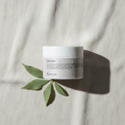 peruda skincare body balm jar with water droplets on a textured white fabric background with green leaves