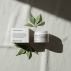 peruda skincare exfoliating mask jar and box with green leaves on a textured white fabric background