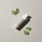 peruda skincare face oil bottle with pump dispenser surrounded by green leaves on a textured beige background