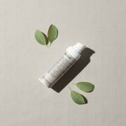 peruda skincare face oil bottle with pump dispenser surrounded by green leaves on a textured beige background