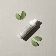 peruda skincare face oil bottle with pump dispenser surrounded by green leaves on a textured beige background