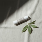 peruda skincare lip balm tube with a green leaf on a textured beige fabric background